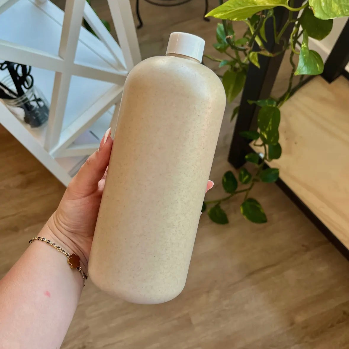 Hand holding a large beige bottle with a white cap indoors.