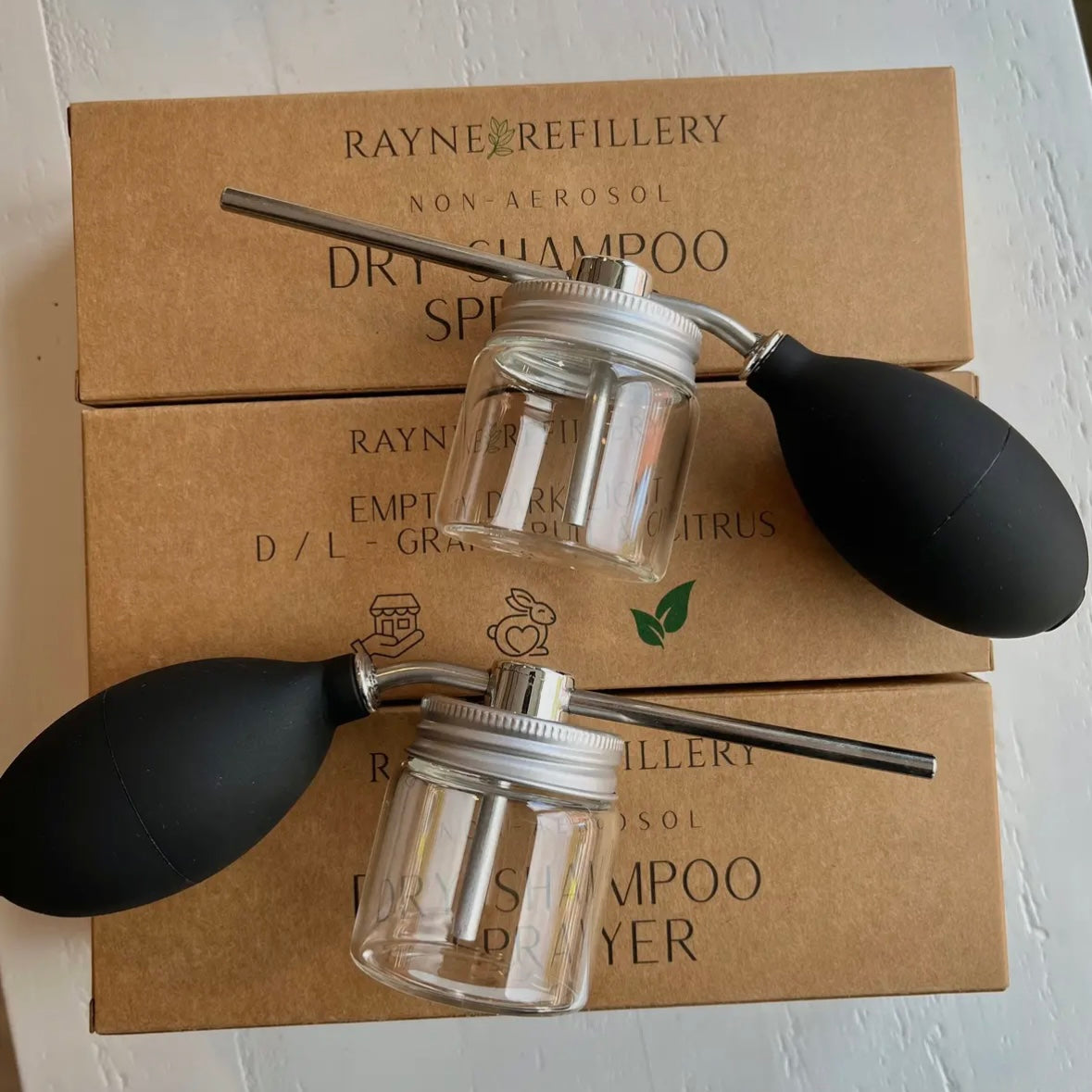 Dry shampoo sprayer with two clear jars on a cardboard box from Rayne Refillery.