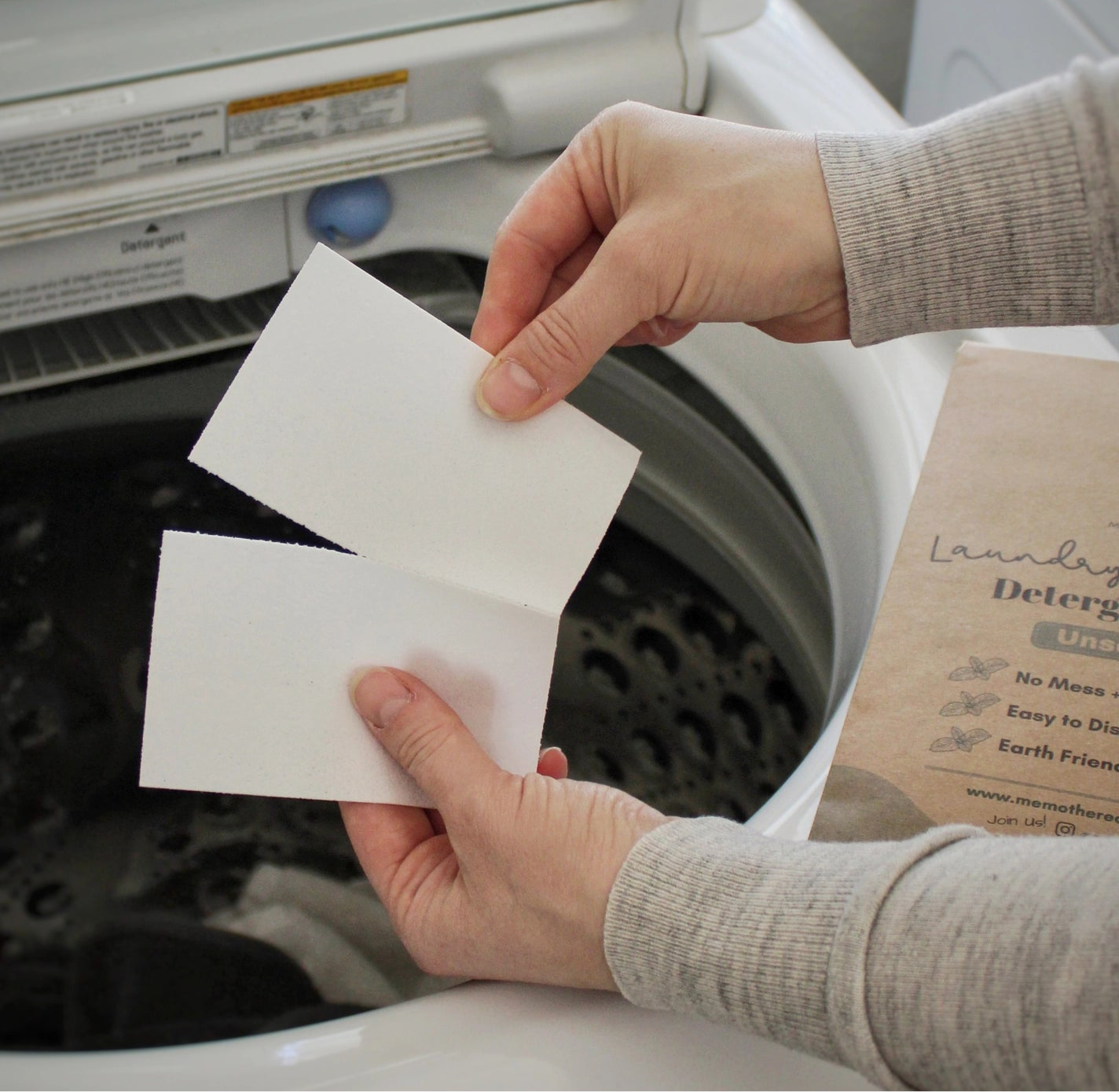 Person ripping laundry sheet in half to put in washing machine. 