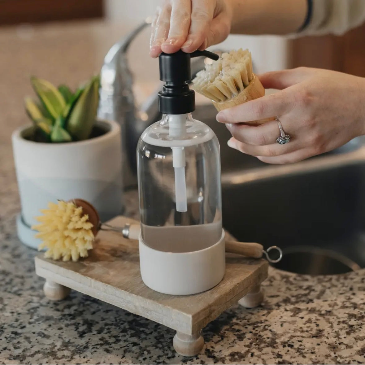 Person using a clear bottle with a pump, the bottle has a beige silicone sleeve covering the bottom portion and base.