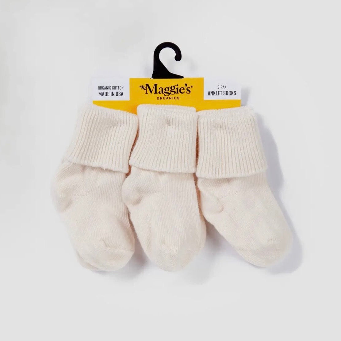 Three pairs of white baby ankle socks on a hanger with 'Maggie's Organics' label.