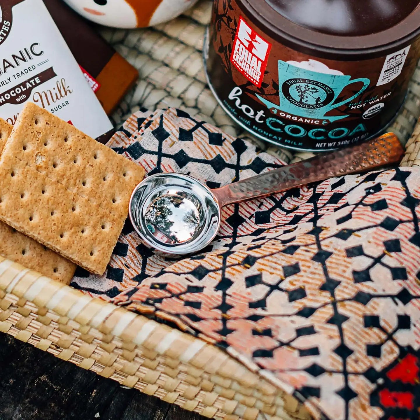 Hot cocoa mix, graham crackers, and a spoon on a patterned surface