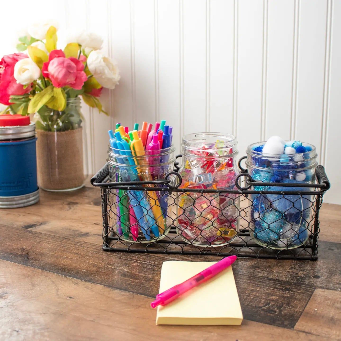 Slotted chicken wire basket on desk holding jars of stationery supplies..